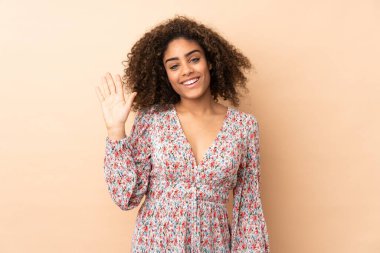Genç Afrikalı Amerikalı kadın bej arka planda izole edilmiş, mutlu bir ifadeyle selamlanıyor.