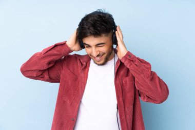 Arap yakışıklı adam mavi arka planda izole edilmiş müzik dinliyor.