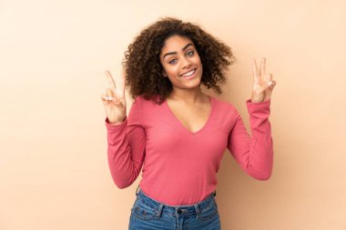 Bej arka planda izole edilmiş genç Afrikalı Amerikalı kadın iki eliyle zafer işareti gösteriyor.