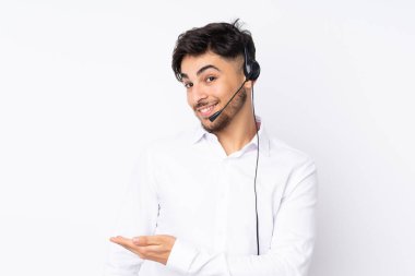 Tele pazarlamacı Arap bir adam beyaz arka planda izole edilmiş bir kulaklıkla çalışıyor. Gelmesi için ellerini yana uzatıyor.