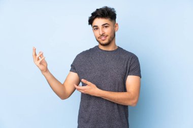 Arap yakışıklı adam soyutlanmış arka planda. Davet edilmek için ellerini yana uzatıyor.
