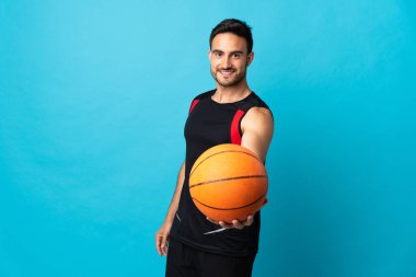 Genç yakışıklı adam mavi arka planda izole edilmiş basketbol oynuyor.