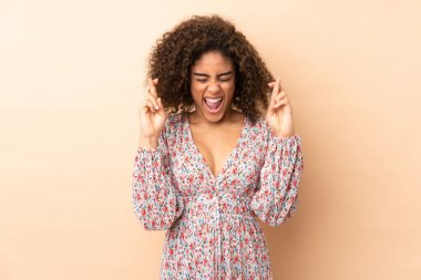 Genç Afrikalı Amerikalı kadın bej arka planda izole edilmiş ve parmakları çapraz