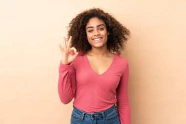 Genç Afrikalı Amerikalı kadın bej arka planda izole edilmiş. Parmaklarıyla işaret veriyor.