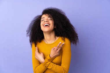 Mor arka planda izole edilmiş genç Afrikalı Amerikalı kadın gülümsüyor ve zafer işareti gösteriyor.