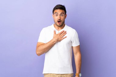 Mor arka planda soyutlanmış yakışıklı genç adam şaşırmış ve şaşırmış görünüyor.