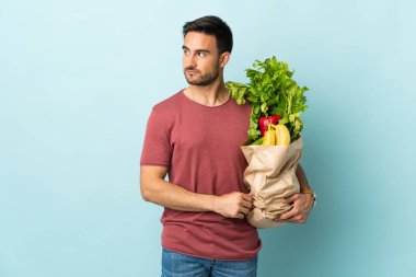 Kafkasyalı genç bir adam mavi arka planda izole edilmiş sebze alıyor.