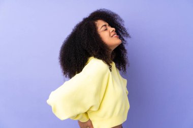 Genç Afrikalı Amerikalı kadın, mor arka planda izole edilmiş, gayret gösterdiği için sırt ağrısı çekiyor.