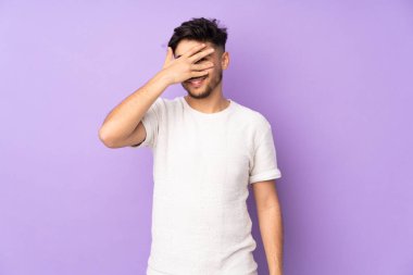 İzole edilmiş arka planda yaşayan yakışıklı Arap bir adam. Gözleri elleriyle kaplıyor ve gülümsüyor.
