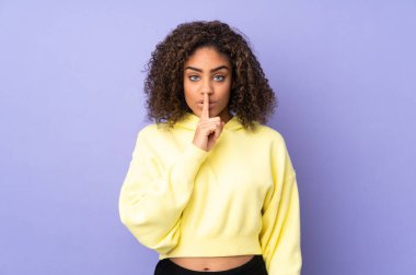 Genç Afrikalı Amerikalı bir kadın arka planda izole edilmiş. Sessiz bir jest işareti var. Parmağını ağzına sok.