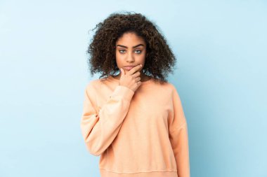 Genç Afrikalı Amerikalı kadın mavi arka planda izole edilmiş düşünüyor.
