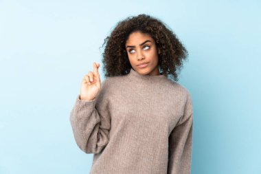 Genç Afrikalı Amerikalı kadın, mavi arka planda izole edilmiş, şans diliyor ve en iyisini diliyor.