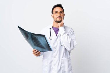 Genç bir doktor elinde beyaz arka planda izole edilmiş bir radyografi tutarak bir fikir düşünüyor.