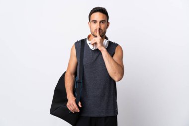 Spor çantalı genç adam beyaz arka planda izole edilmiş. Parmağını ağzına koyduğunda sessizlik işareti gösteriyor.