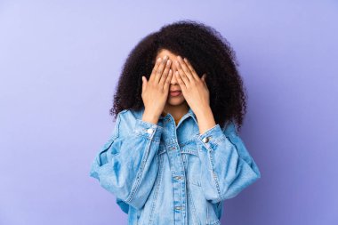 Genç Afrikalı Amerikalı kadın mor arka planda izole edilmiş gözleri elleriyle kapatıyor.
