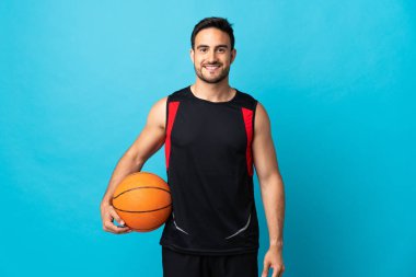 Genç yakışıklı adam mavi arka planda izole edilmiş basketbol oynuyor.