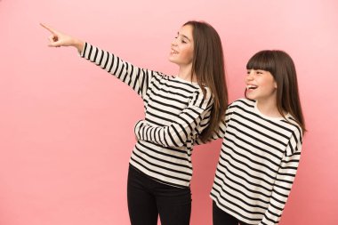 Küçük kız kardeşler pembe arka planda izole edilmiş bir şekilde bir fikir sunuyorlar.