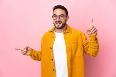 Pembe arka planda izole edilmiş beyaz tenli yakışıklı adam parmak uçlarını işaret ediyor ve mutlu.