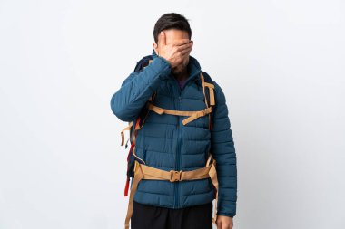 Büyük bir sırt çantası olan genç dağcı, beyaz arka planda izole edilmiş, gözlerini elleriyle kapatıyor.