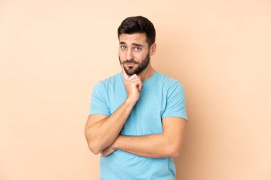 Beyaz tenli yakışıklı adam bej arka planda izole edilmiş ve düşünüyor.