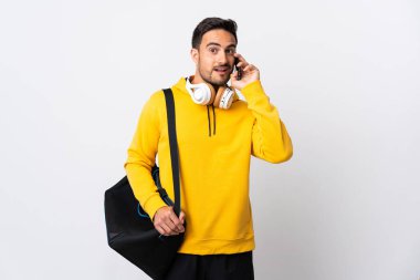 Spor çantalı genç adam beyaz arka planda izole edilmiş cep telefonuyla biriyle sohbet ediyor.