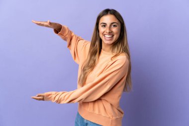 İzole edilmiş mor arka planı olan genç İspanyol kadın bir ilan vermek için kopyalama alanı tutuyor.