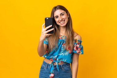 İzole edilmiş sarı arka planda cep telefonu kullanan genç bir kadın.