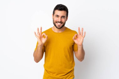 Beyaz arka planda sakallı yakışıklı genç adam iki eliyle tamam işareti gösteriyor.