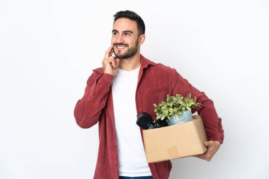 Beyaz arka planda izole edilmiş eşyalarla dolu bir kutuyu kaldırırken genç beyaz bir adam hamle yapıyor.