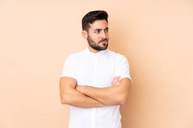 Beyaz tenli yakışıklı adam bej arka planda izole edilmiş ve kollarını kavuşturuyor.