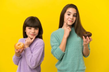 Sarı arka planda izole edilmiş küçük kız kardeşler ellerinde donut tutuyorlar.