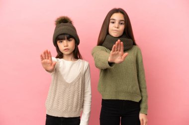 Pembe arka planda izole edilmiş kışlık giysiler giyen küçük kız kardeşler yanlış düşünen bir durumu inkar etmeyi bırakıyorlar.
