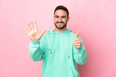 Pembe arka planda izole edilmiş beyaz, yakışıklı genç adam parmaklarıyla altısını sayıyor.