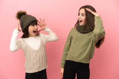 Pembe arka planda izole edilmiş, şaşırmış ve şok olmuş yüz ifadeleri takınan küçük kız kardeşler.