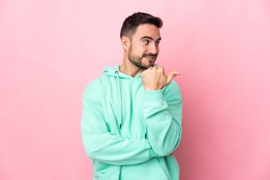 Pembe arka planda izole edilmiş beyaz, yakışıklı genç bir adam bir ürün sunmak için kenarı işaret ediyor.