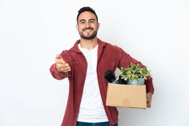 Young caucasian man making a move while picking up a box full of things isolated on white background shaking hands for closing a good deal