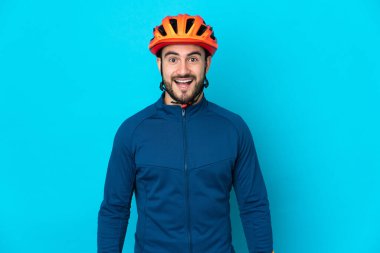 Genç bisikletçi, mavi arka planda izole edilmiş, şaşırmış bir yüz ifadesi var.