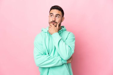 Beyaz tenli yakışıklı bir adam pembe arka planda izole edilmiş, yukarı bakarken bir fikir düşünüyor.