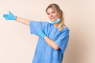 İzole edilmiş arka planda aletleri tutan dişçi kadın davet edilmek için ellerini yana uzatıyor.