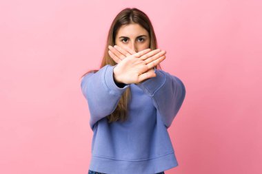 Soyutlanmış pembe arka planı olan genç bir kadın bir hareketi durdurmak için eliyle jest yapıyor.