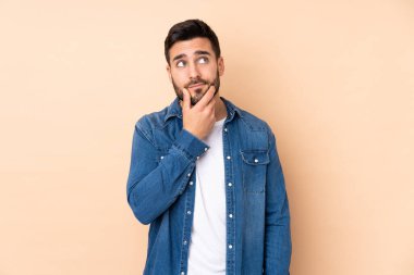 Beyaz tenli yakışıklı adam bej arka planda izole edilmiş. Şüpheleri var ve kafası karışmış bir yüz ifadesi var.