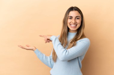 Beyaz tenli genç bir kadın, bej arka planda izole edilmiş. Elinde bir ilan vermek için avuç içi hayali fotokopi makinesi var.