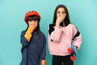 Küçük kız kardeşler bisiklete biniyor ve kaykaycı mavi arka planda izole edilmiş ağzı ellerle kapatıyor uygunsuz bir şey söylediği için.