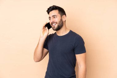 Beyaz tenli yakışıklı adam bej arka planda izole edilmiş cep telefonuyla sohbet ediyor.