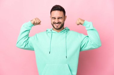 Pembe arka planda izole edilmiş beyaz, yakışıklı genç bir adam güçlü bir jest yapıyor.