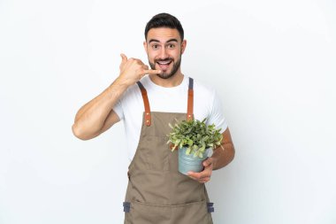 Bahçıvan beyaz arka planda izole edilmiş bir bitki tutuyor ve telefon jesti yapıyor. Bana geri dönüş işareti ver.