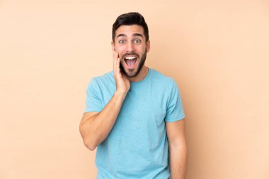 Beyaz tenli yakışıklı, bej arka planda izole edilmiş, şaşırmış ve şok olmuş bir yüz ifadesi var.