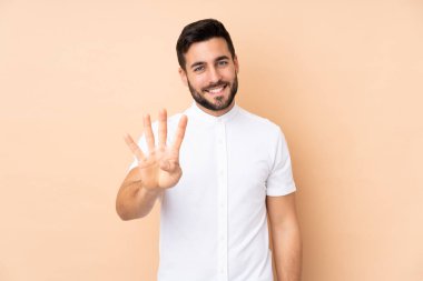 Beyaz tenli yakışıklı adam bej arka planda izole edilmiş mutlu ve parmaklarıyla dört kişi sayıyor.