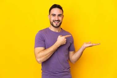 Beyaz, yakışıklı, sarı arka planda izole edilmiş genç bir adam. Avucunun içinde hayali bir fotokopi makinesi tutuyor.