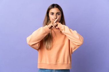 Tecrit edilmiş mor arka planda genç bir İspanyol kadın sessizlik işareti gösteriyor.